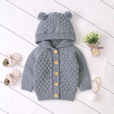 Gray knitted baby cardigan with bear ears on a white wooden floor.